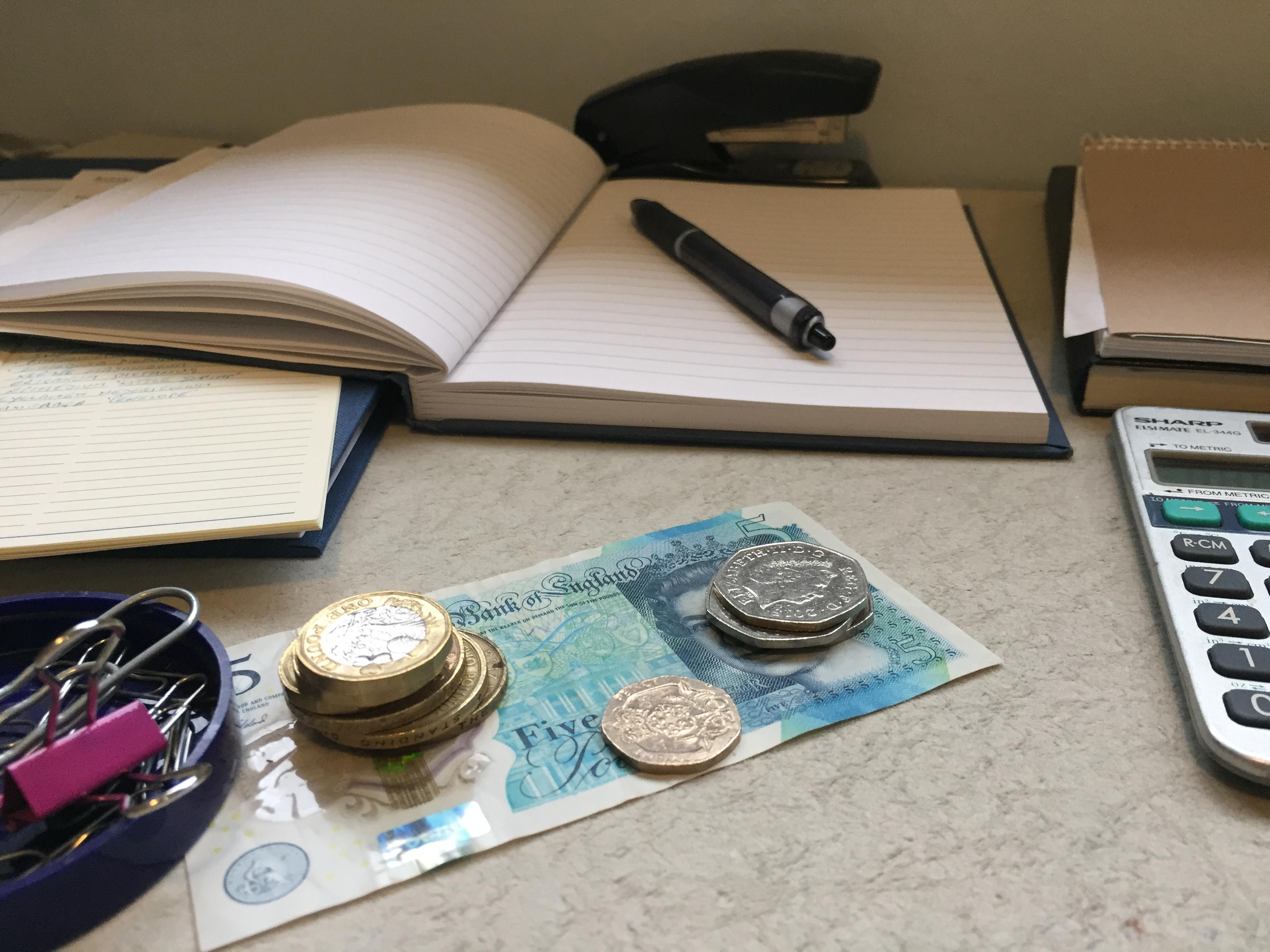 Photo of various objects linked to finance, for example coins, banknotes, books, pen, calculator.